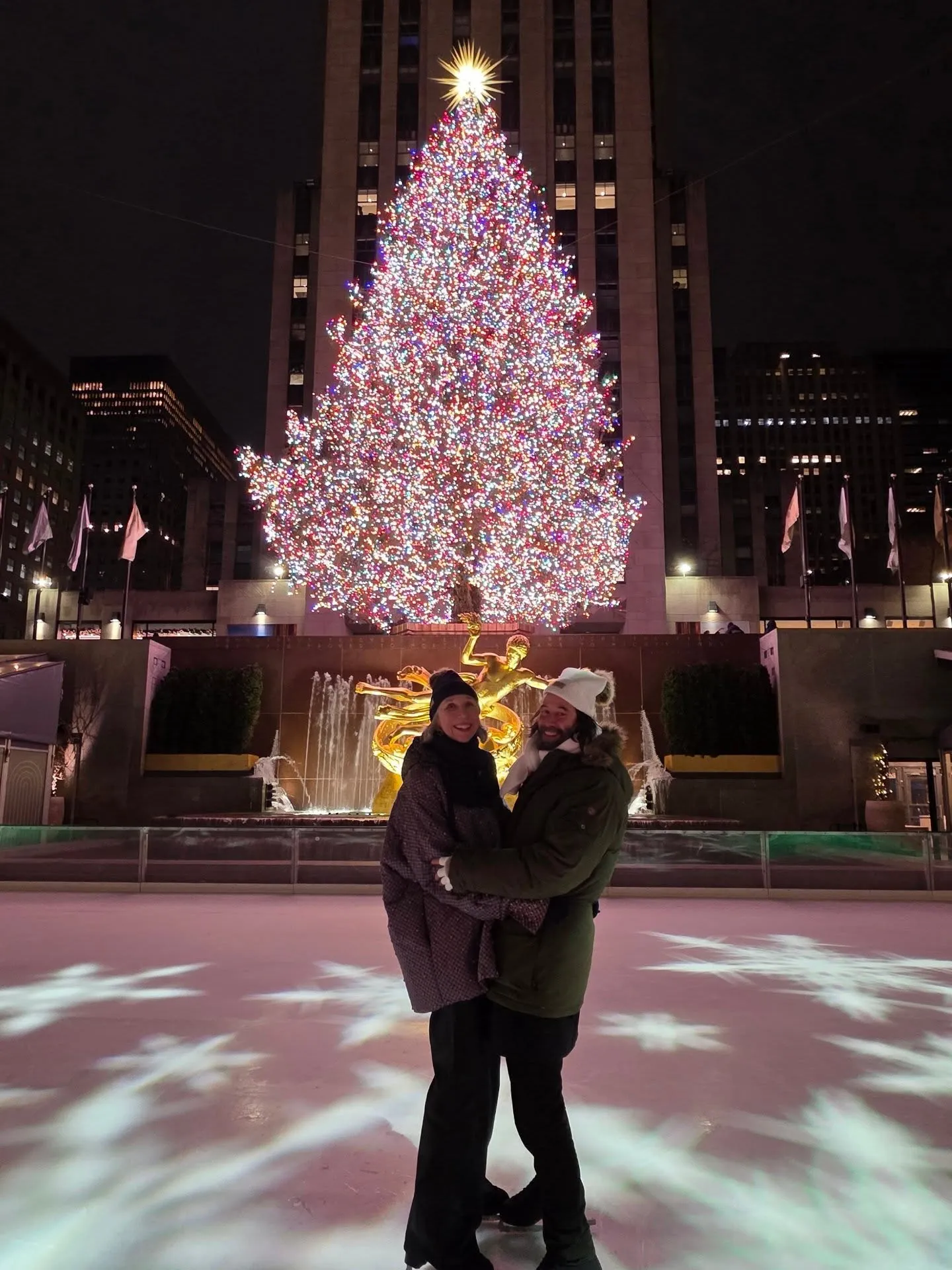 Keanu Reeves and Alexandra Grant ice skating in front of a Christmas tree.