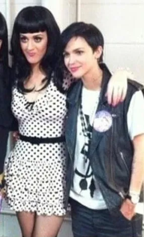 Katy Perry in a white and black polka dot dress posing with Ruby Rose wearing a black vest and white shirt.