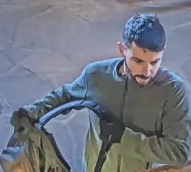 Man with short black hair and beard holding a dark backpack.