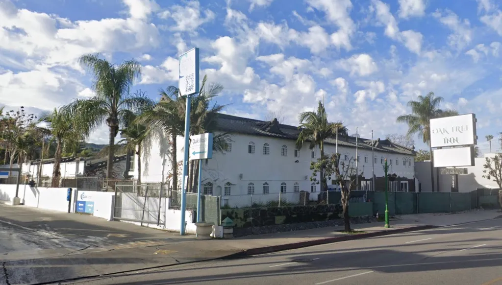 Exterior view of the Oak Tree Inn, a white building with several palm trees, and signs for 