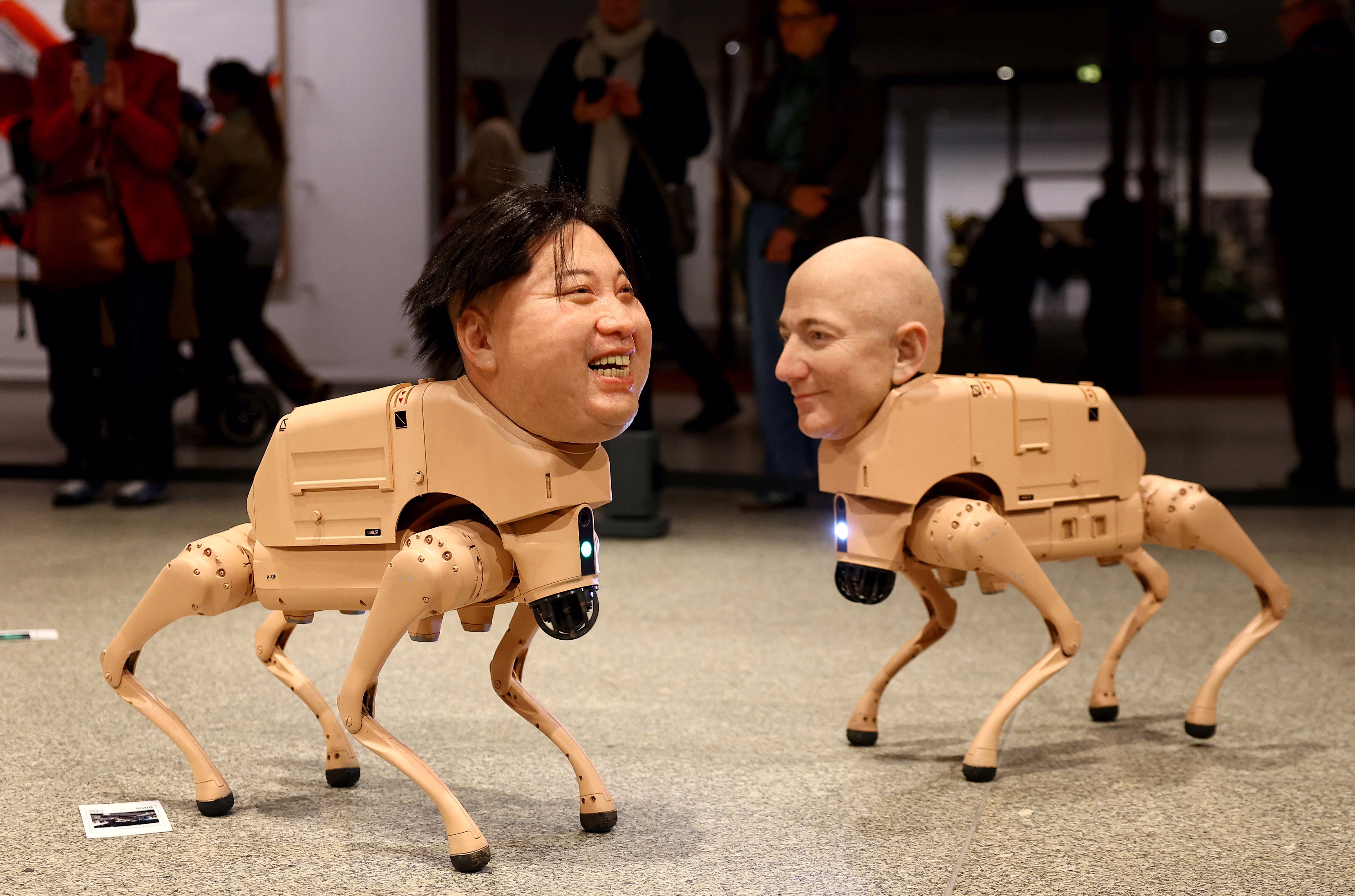 Robotic dogs with silicone heads modeled after Kim Jong Un and Jeff Bezos move about in an interactive art installation.