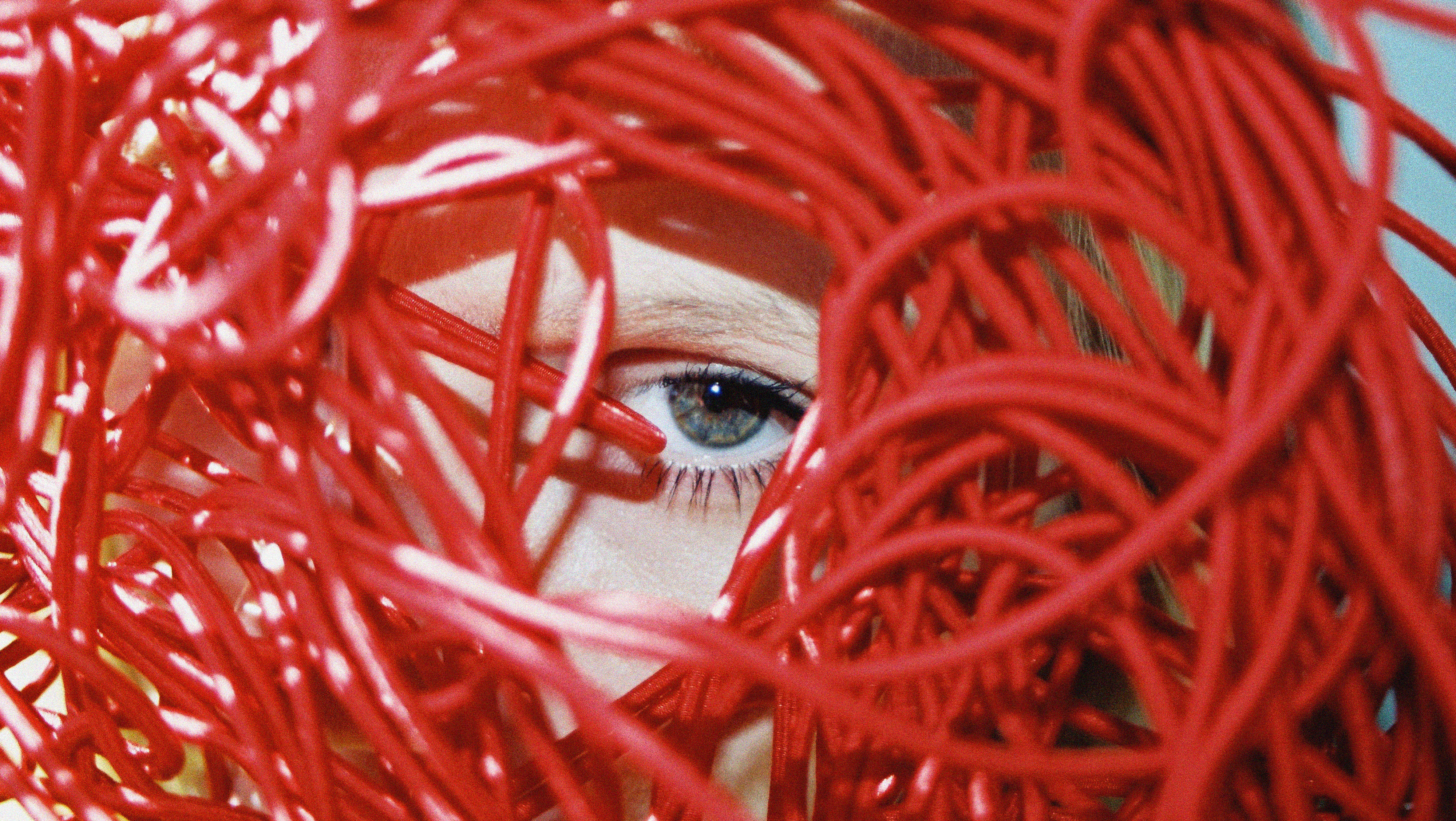 An eye peering through a tangle of red wires