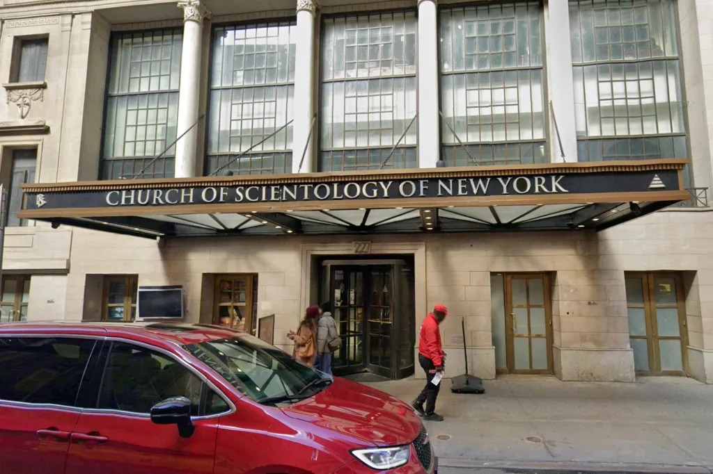 The exterior of the Church of Scientology of New York building with a red minivan parked in front.