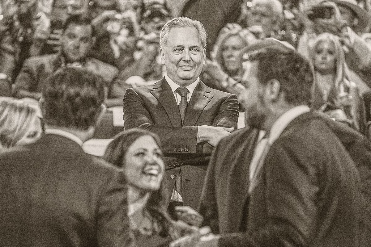 photo of convention with large audience behind David Sacks, smiling and standing with arms crossed in front center, with Vance and others talking in foreground