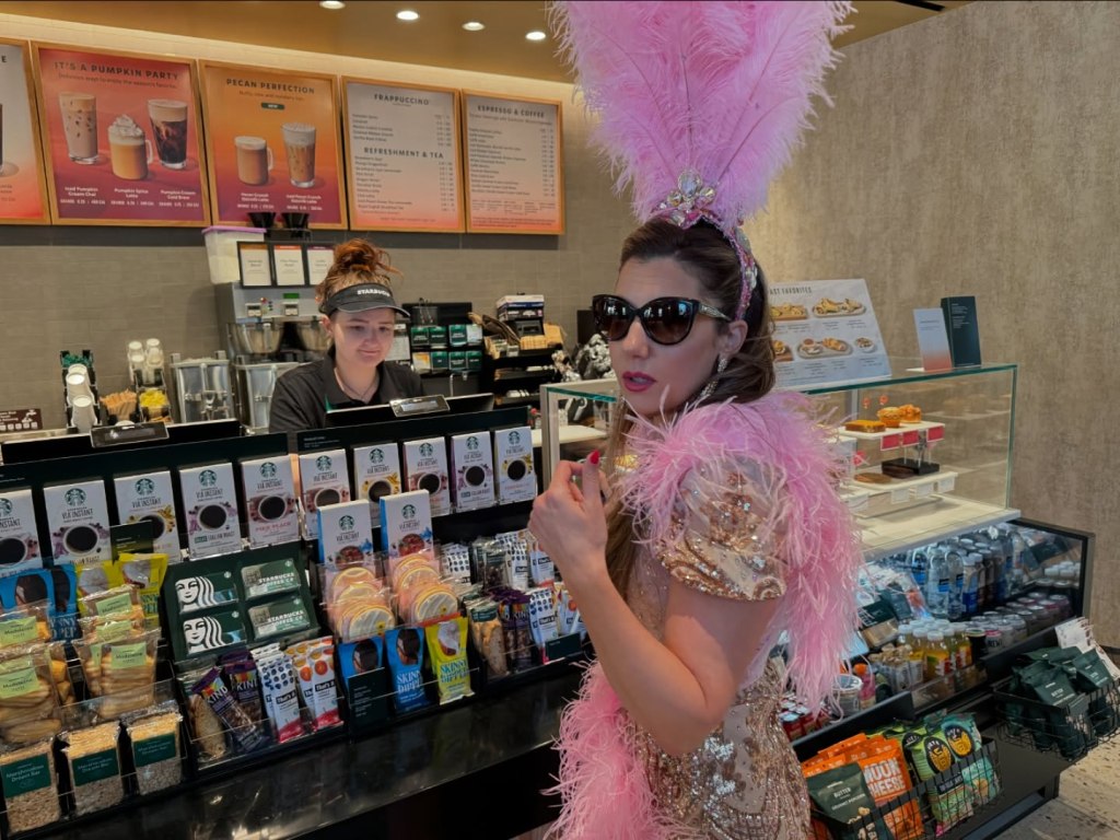 Maren Flagg in a showgirl outfit inside a Starbucks, with a barista in the background.