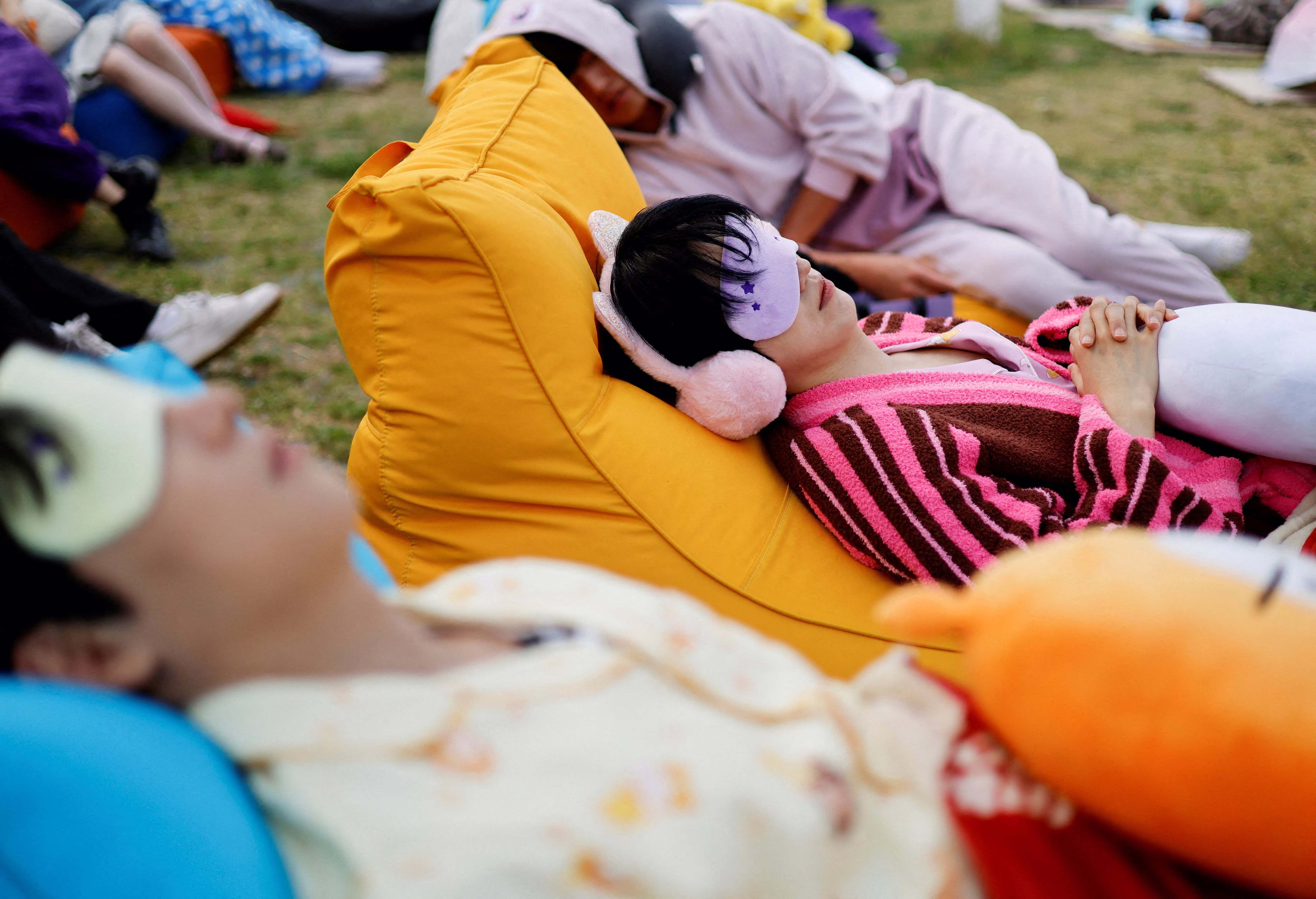 Several people nap together outside, wearing masks over their eyes, during a napping contest.