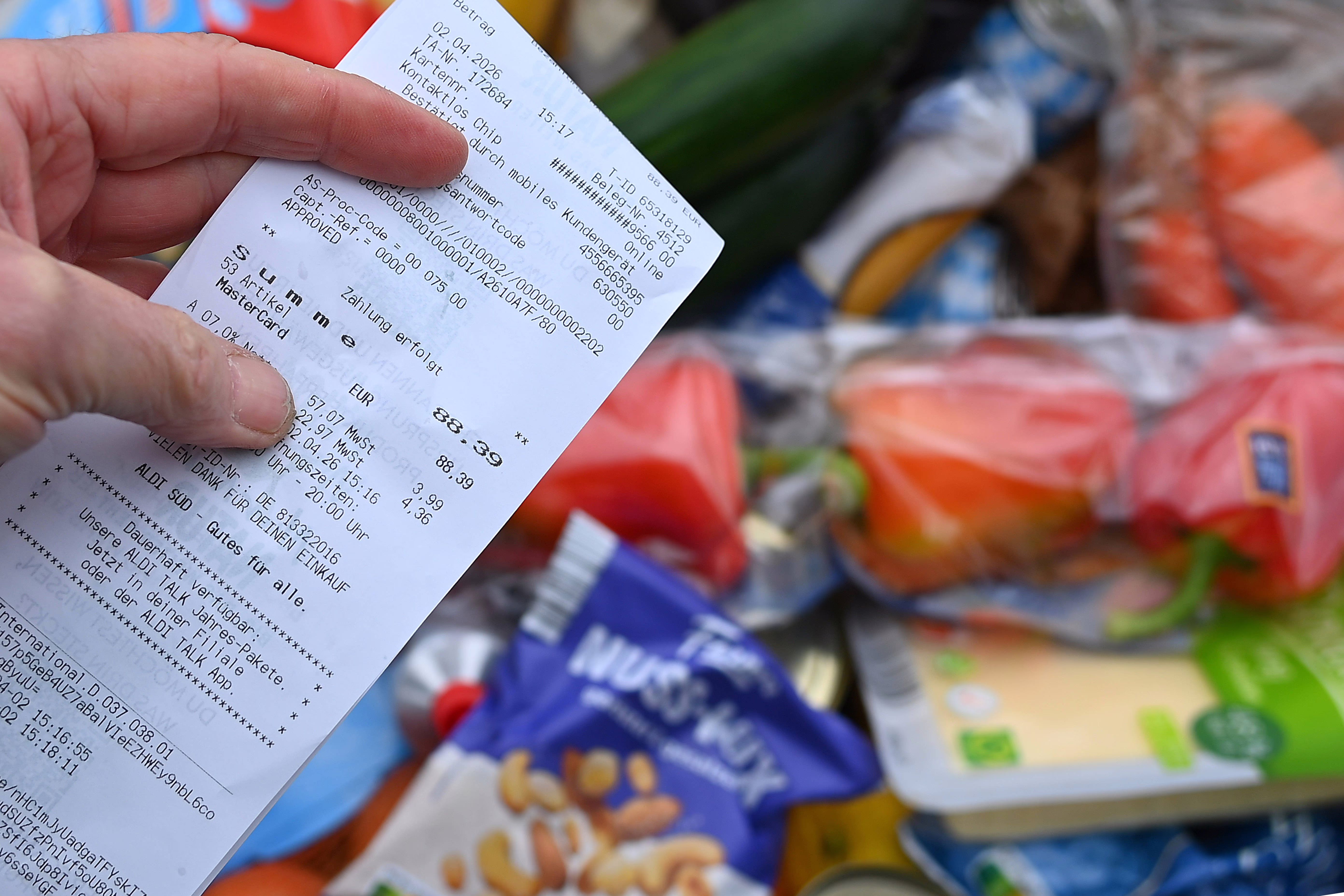 A person holds up a receipt, above a pile of groceries.