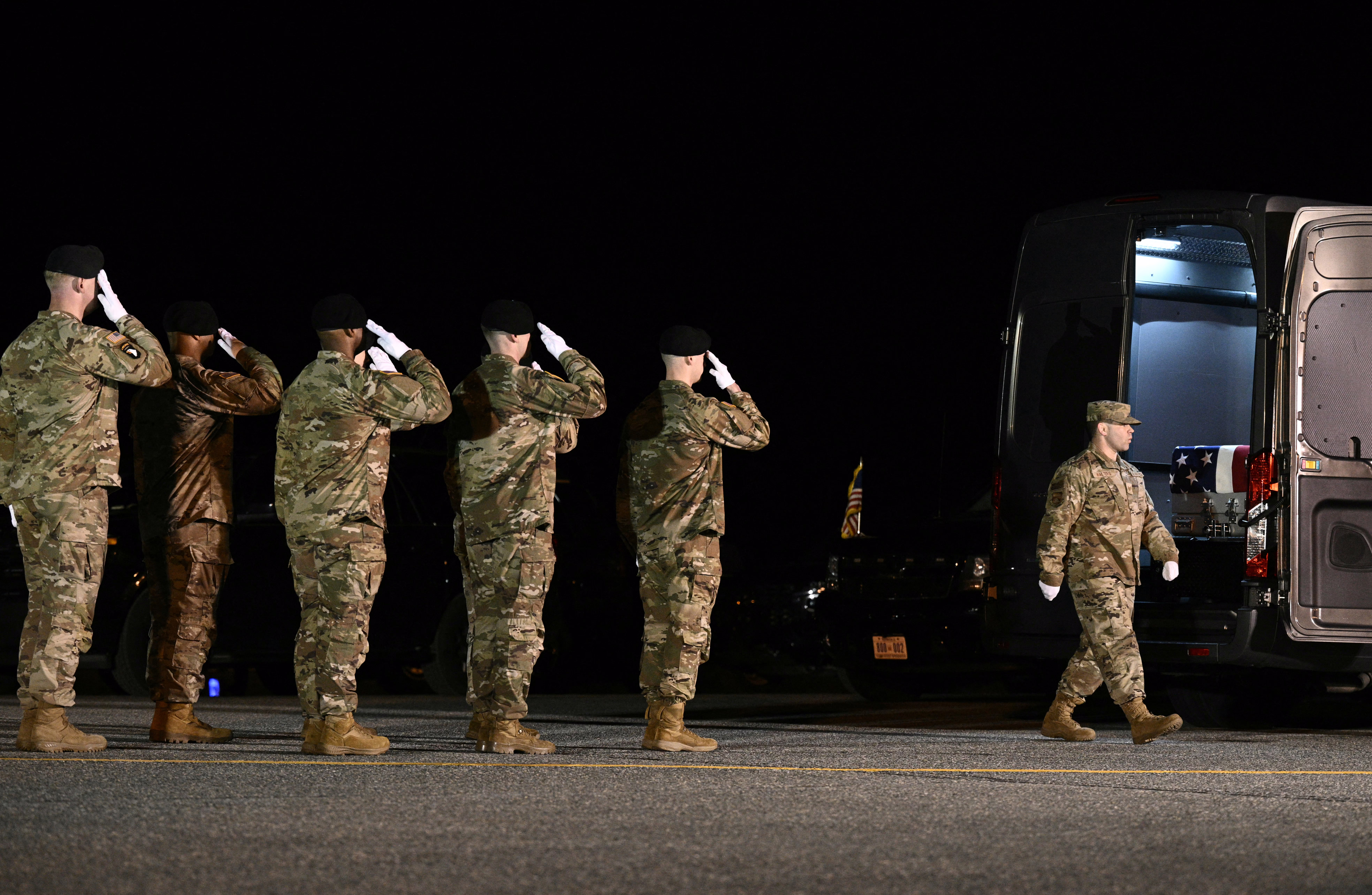 Members of a U.S. Army carry team salute as a flag-draped coffin is moved into a vehicle.