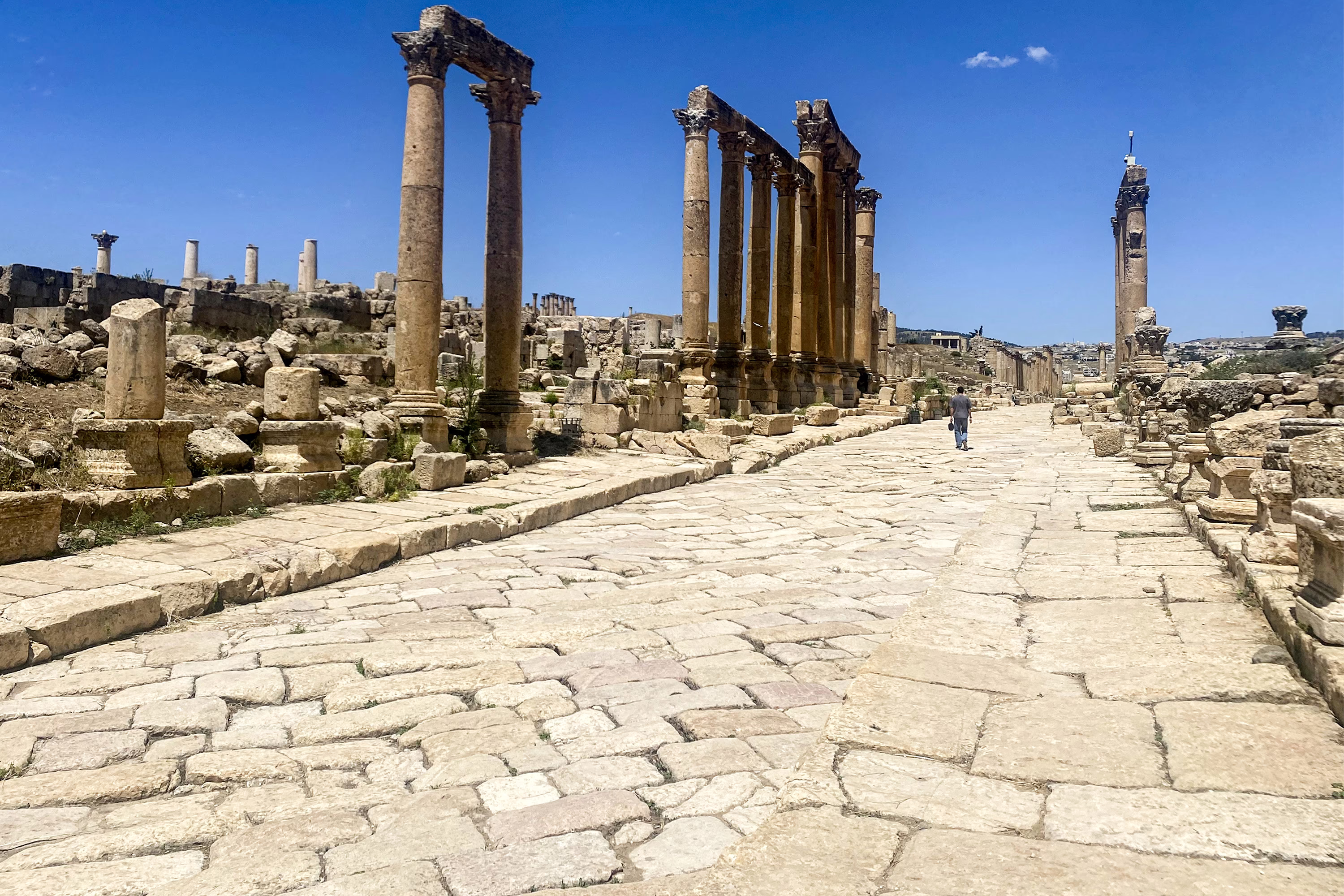 A man walks along a deserted road among ancient Roman ruins.