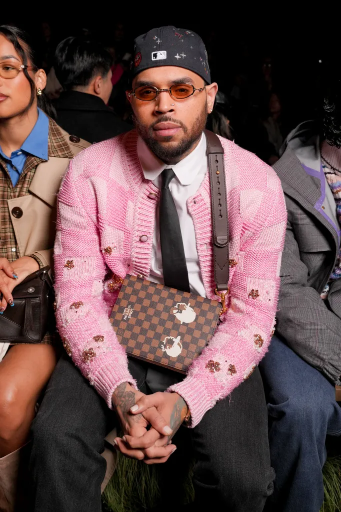 Chris Brown wearing a pink knitted cardigan, black tie, and a Louis Vuitton shoulder bag at the Louis Vuitton Men's Fall/Winter 2026 fashion show.