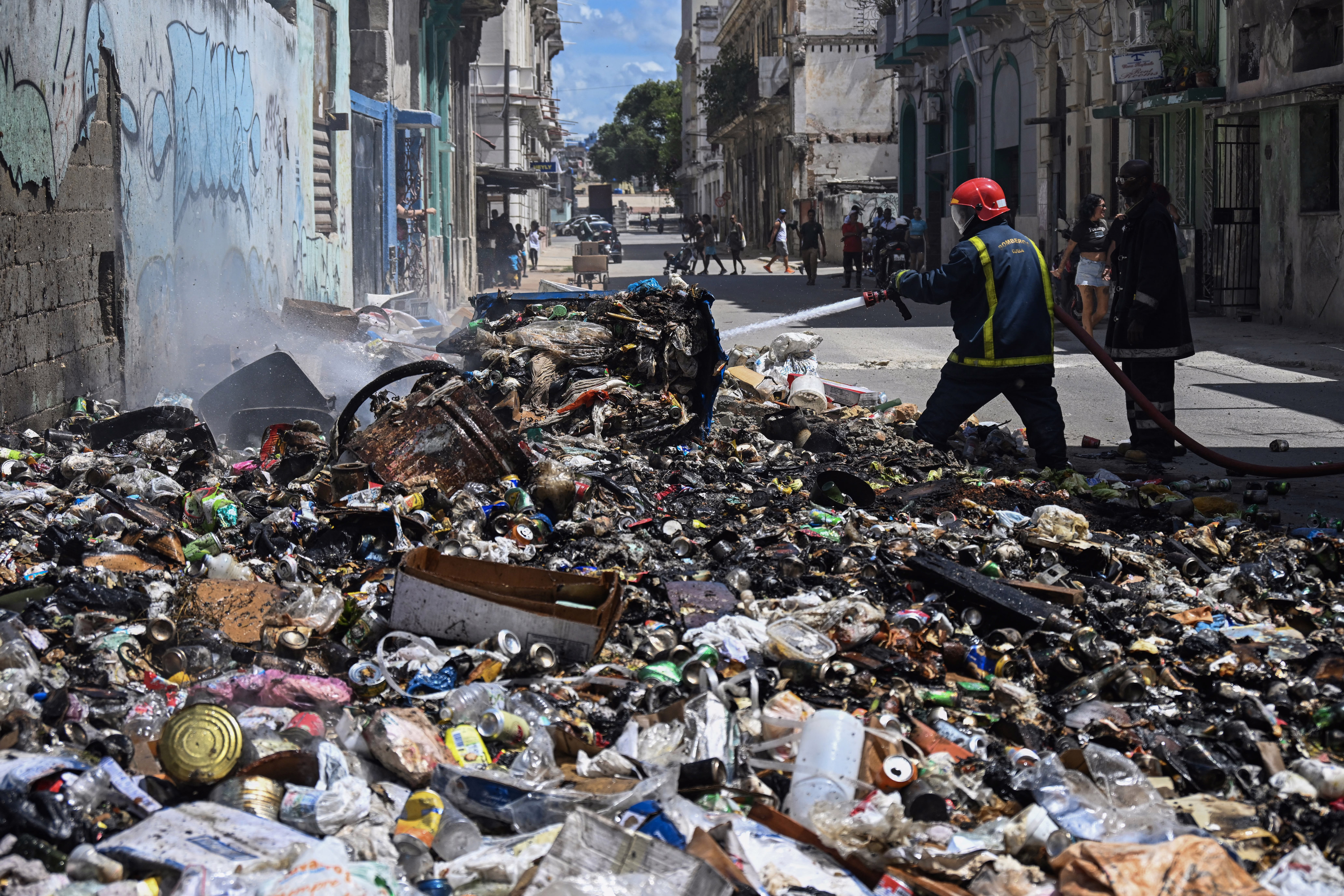 Firefighters work to put out a fire in a large pile of garbage in a street.