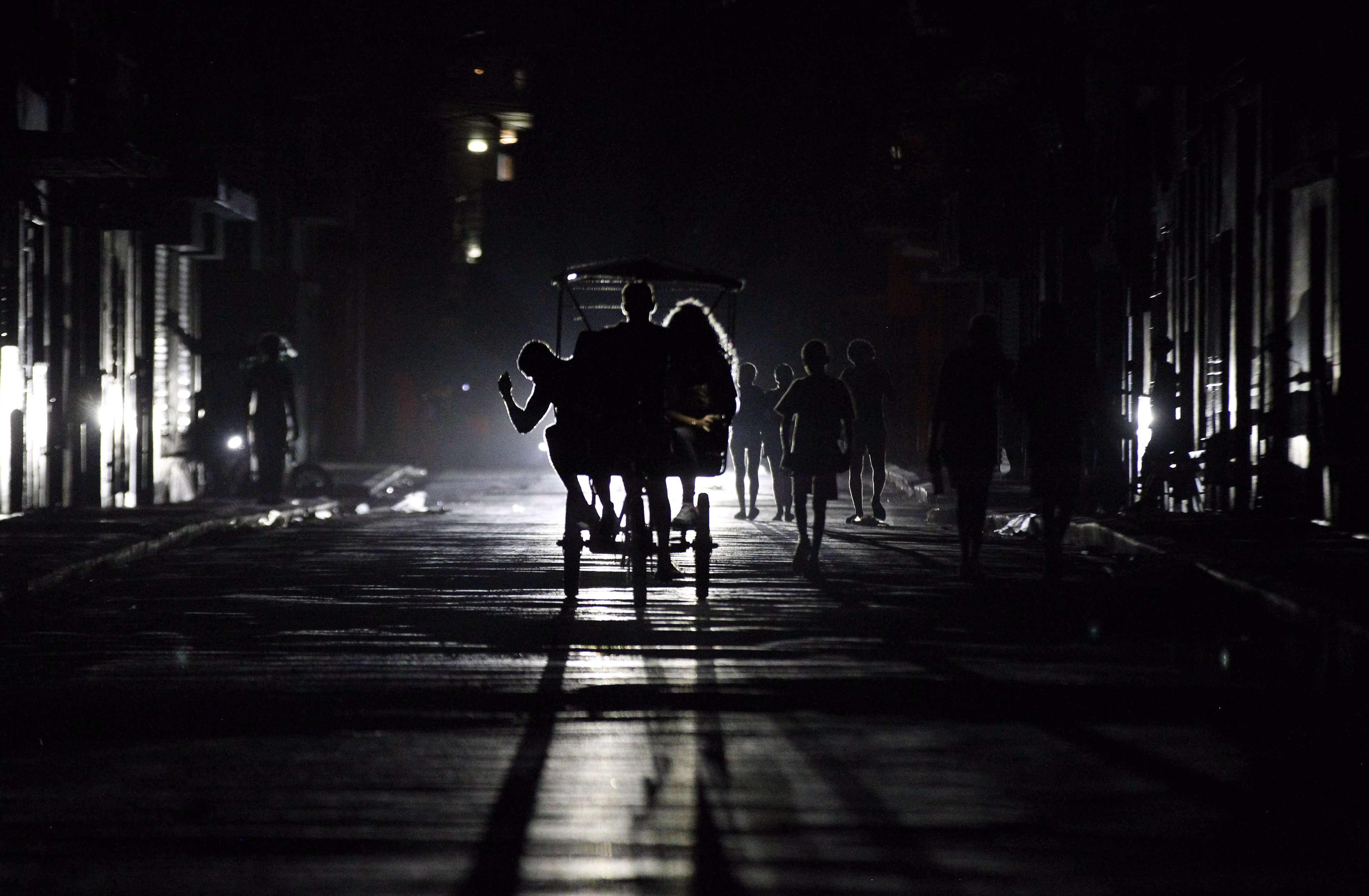 People ride a pedal taxi at night during a blackout.