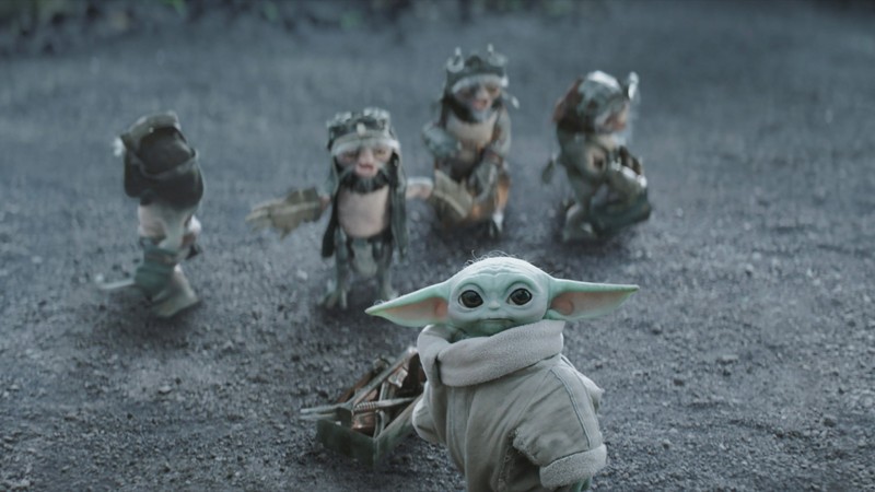 Grogu and four frog-like creatures in helmets stand on grey dirt.