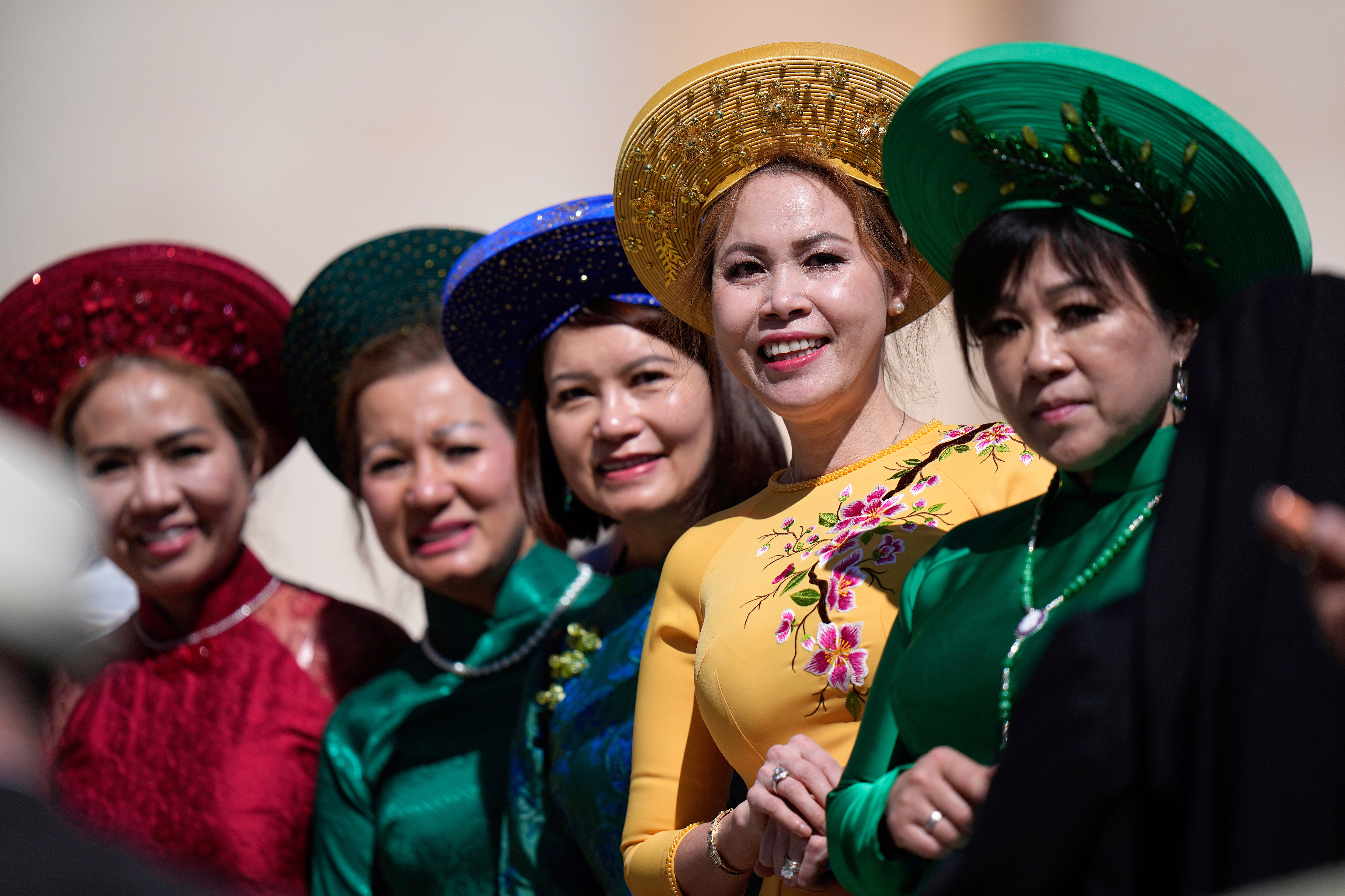 A group of five women wearing colorful traditional Vietnamese outfits and hats