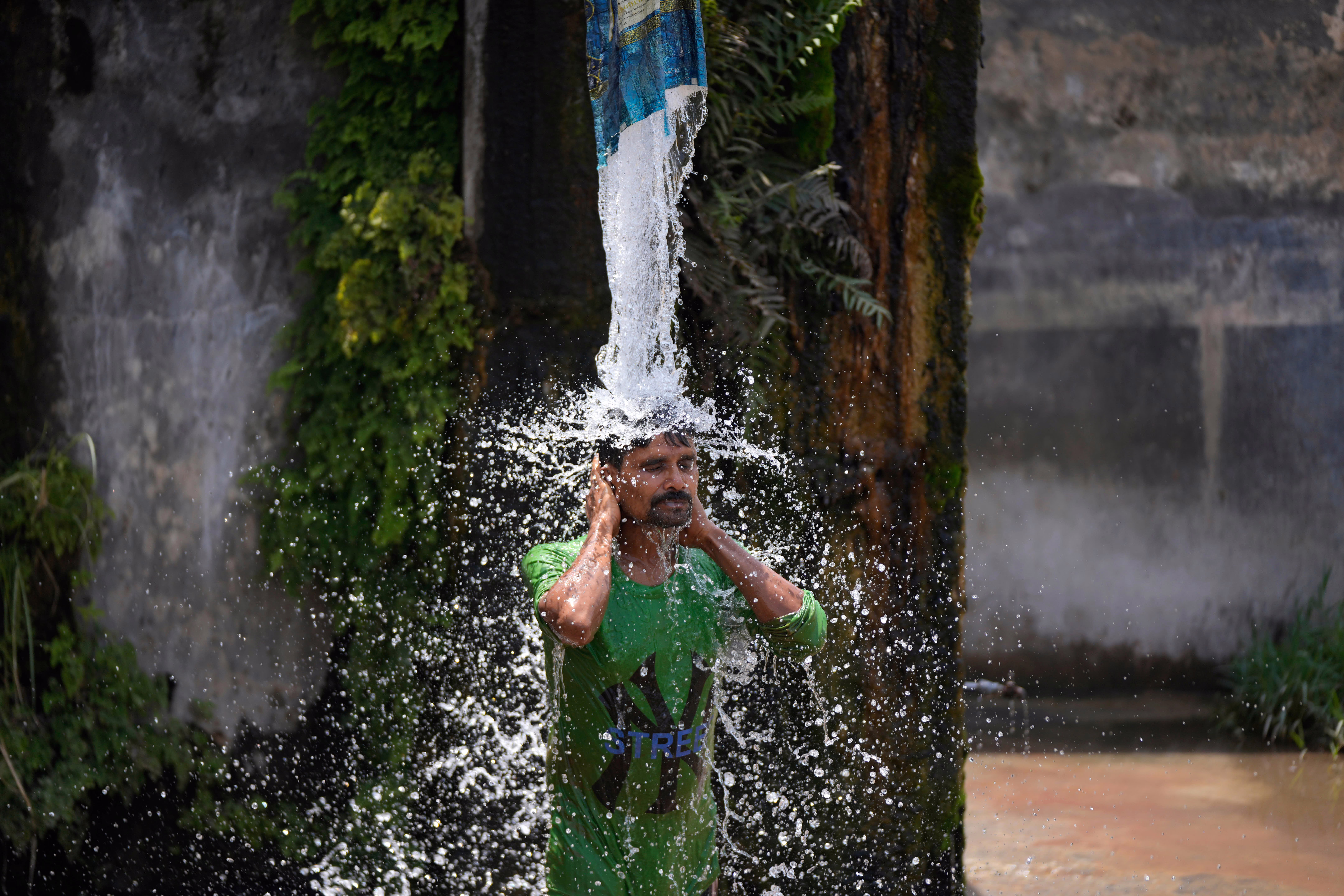 A man stands beneath a water pipe, dousing himself on a hot day.