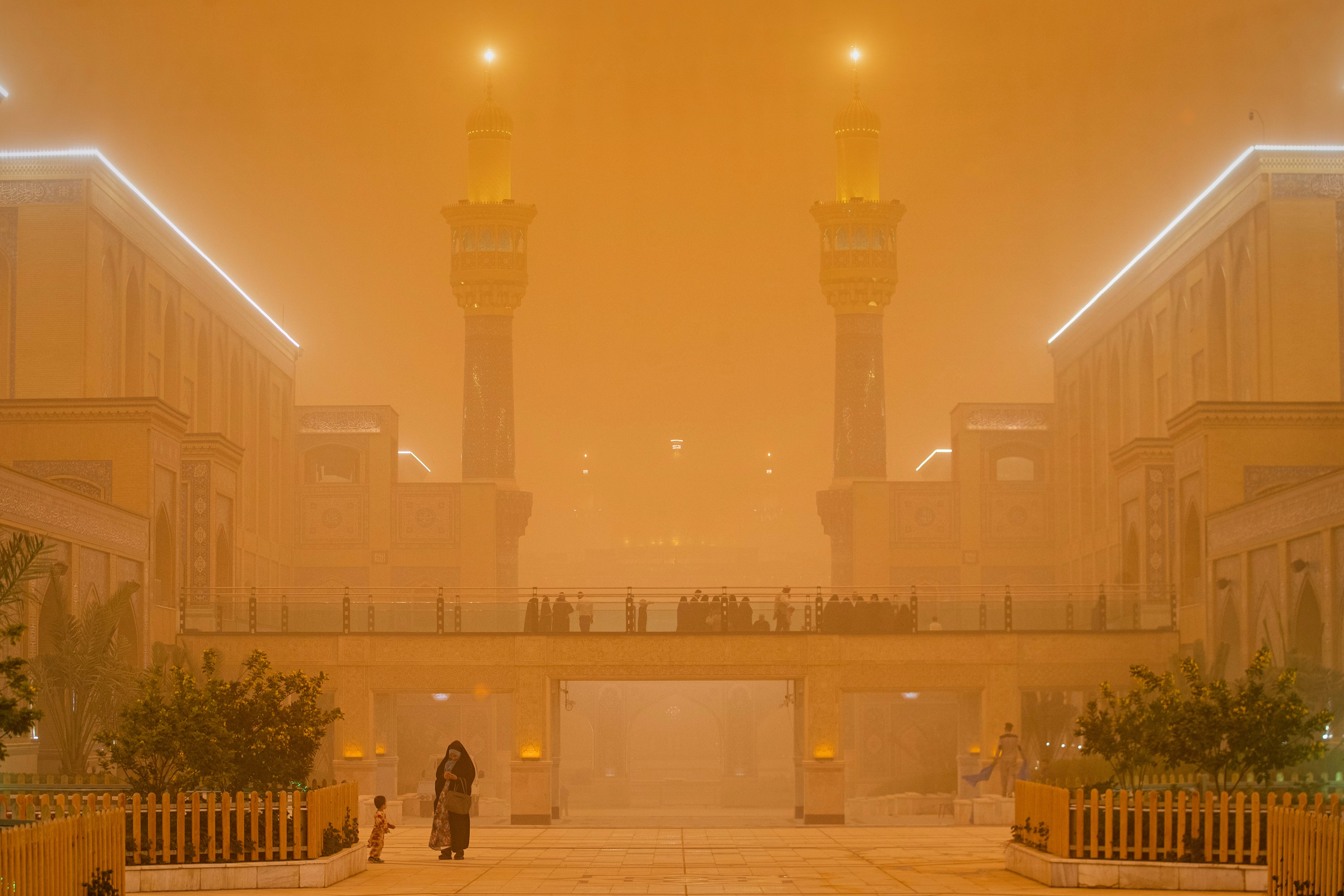 People walk near a shrine during a heavy dust storm, under an orange-colored sky.