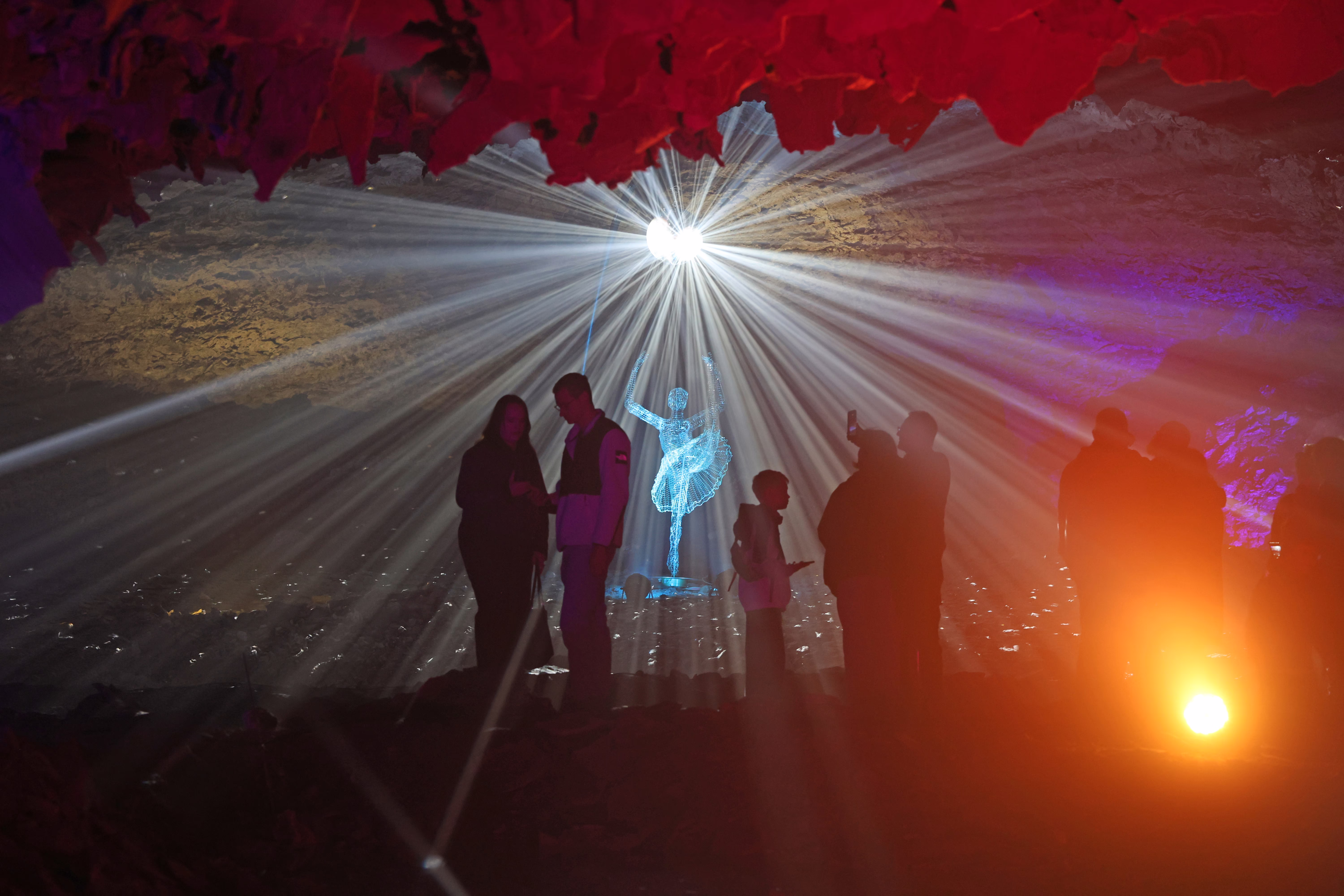 People walk through a cave amid a light show.