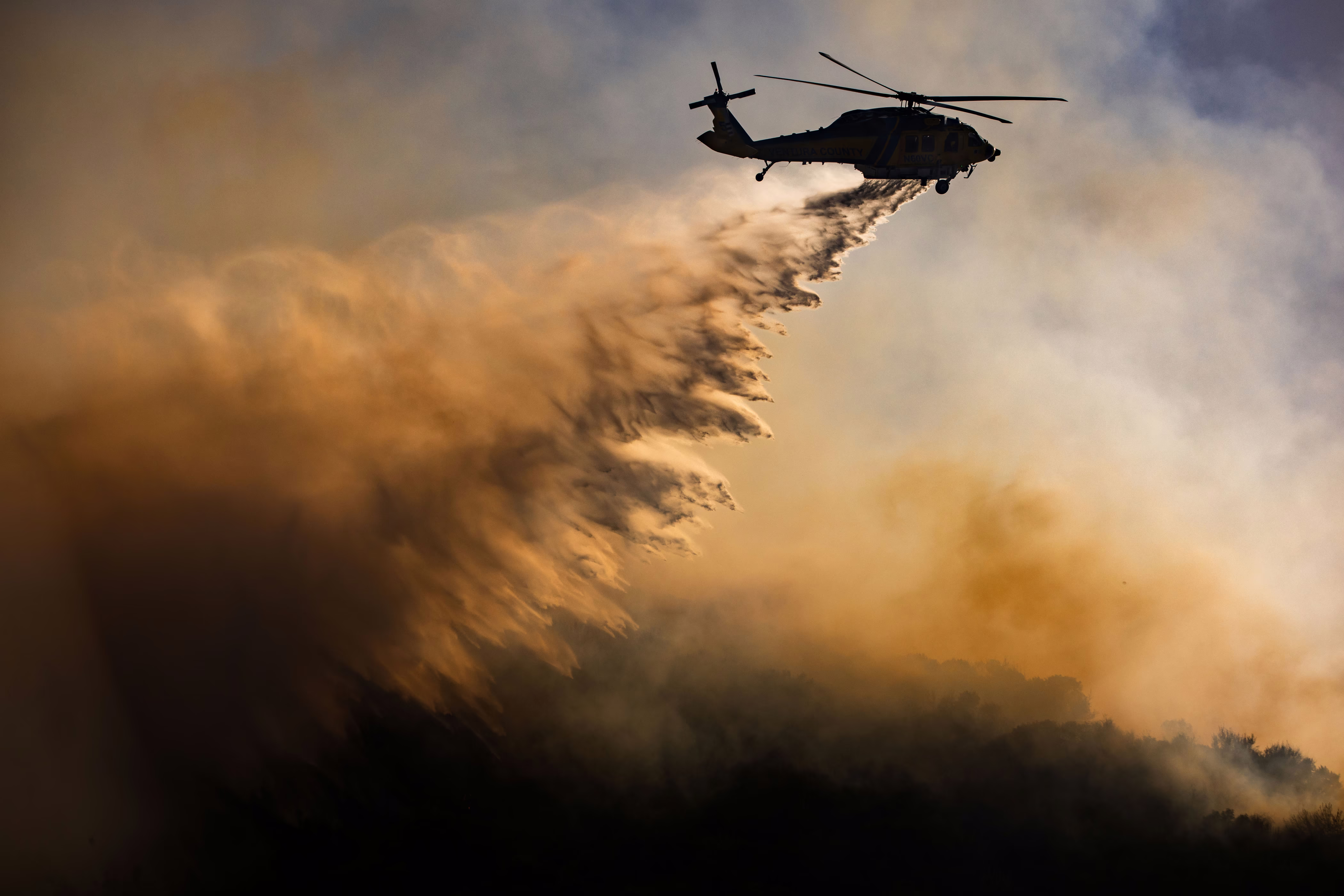 A helicopter drops water on a wildfire.