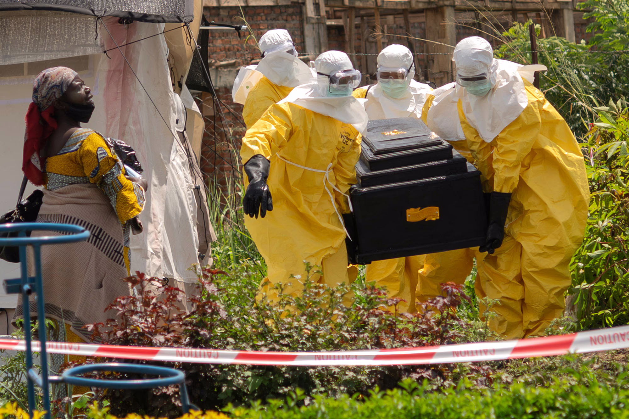Workers wearing heavy protective suits carry a coffin outside a tent at a health-care center.