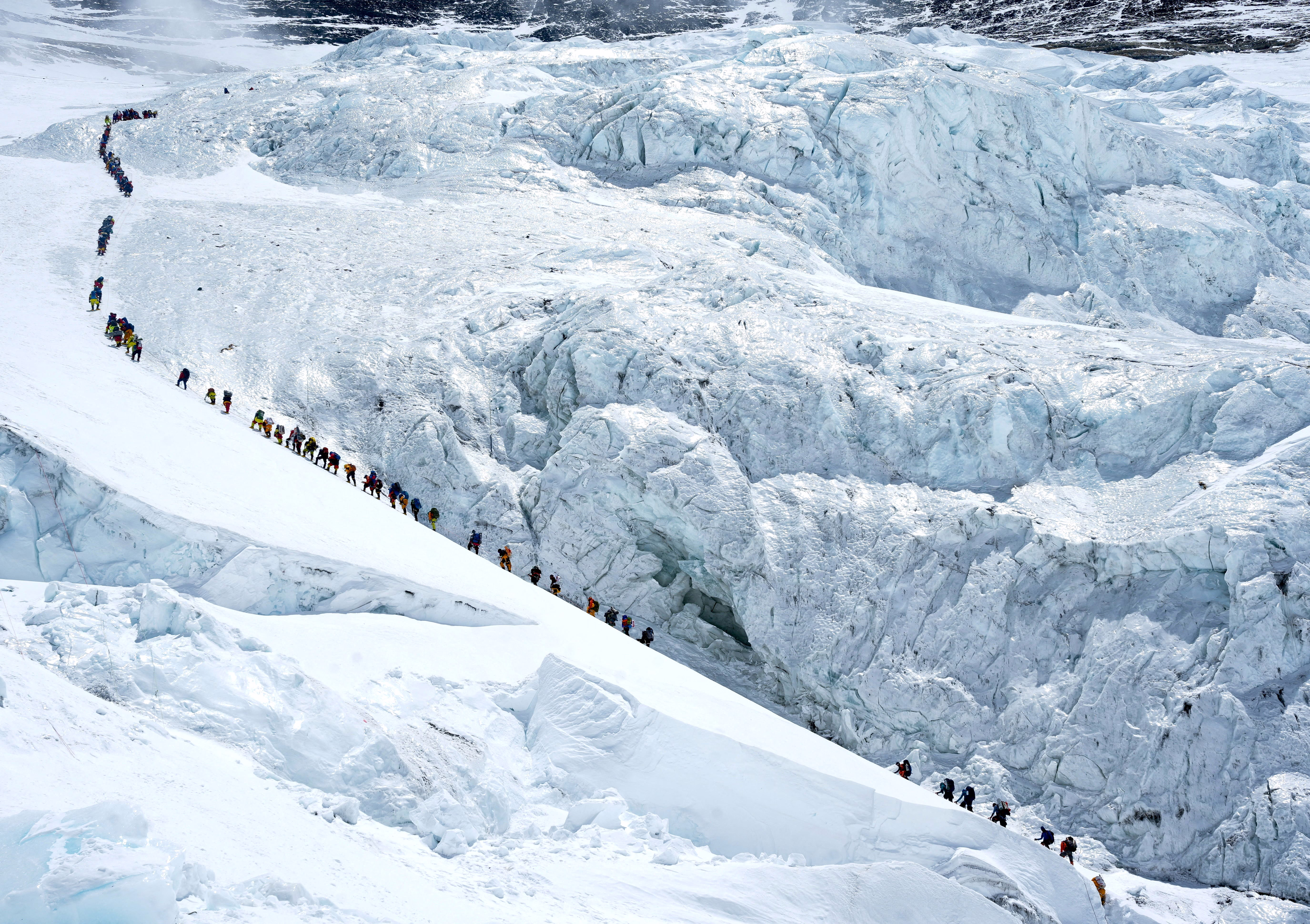 A long line of climbers walk up a steep slope along a glacier on Mount Everest.