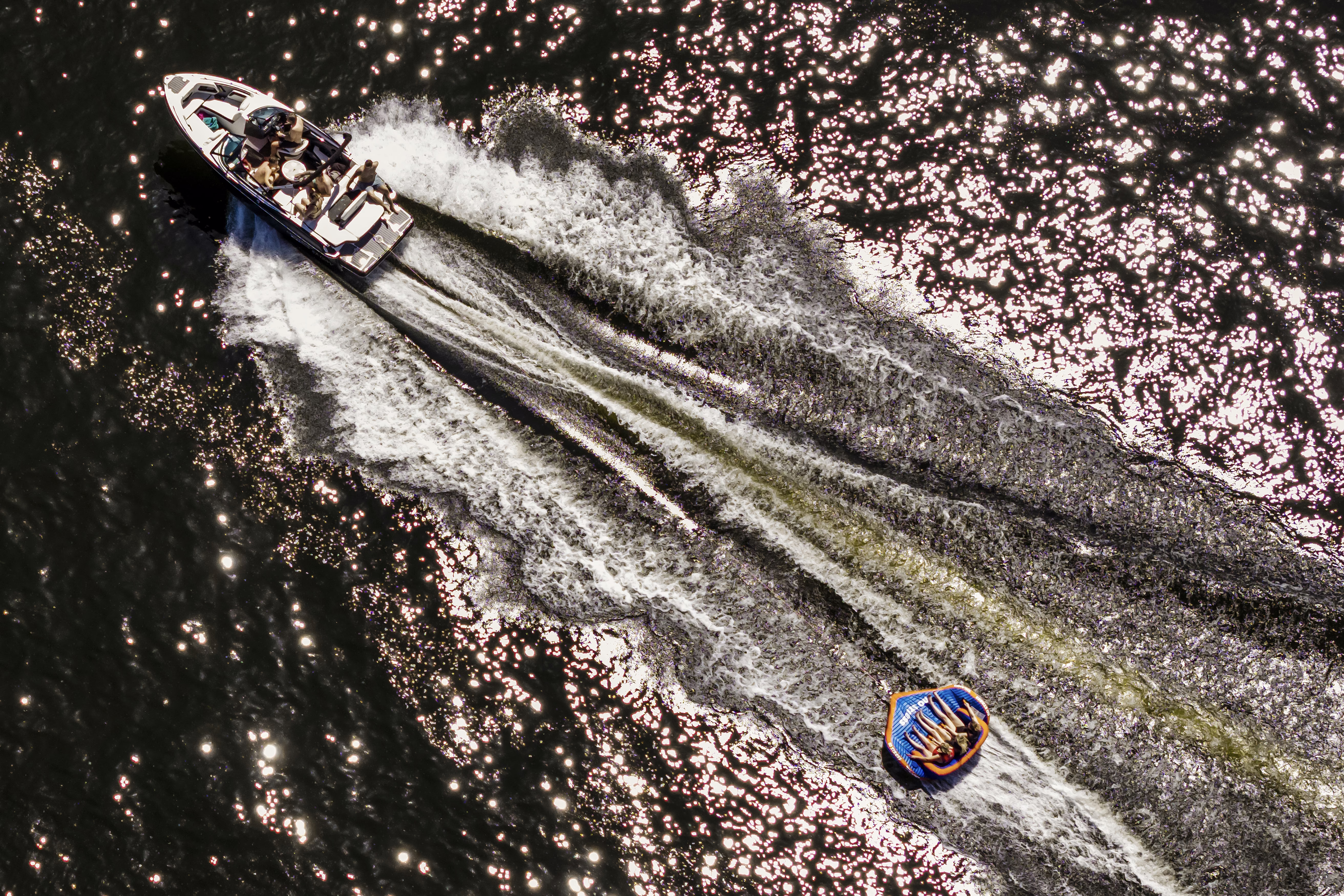 An aerial photograph of people being pulled on an inflatable raft by a motorboat on a lake