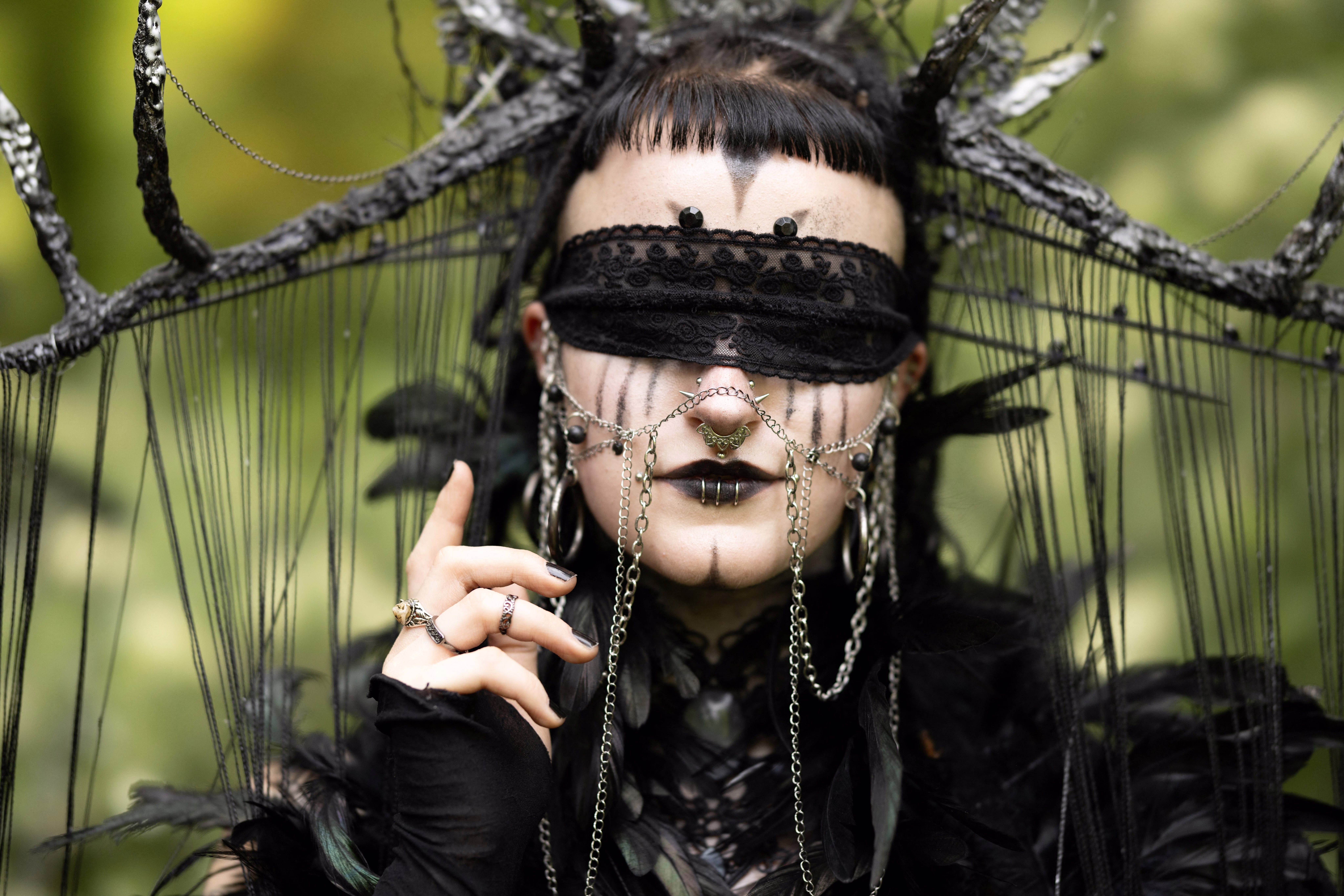 A person poses while wearing dark makeup and dark ornate clothing and accessories.