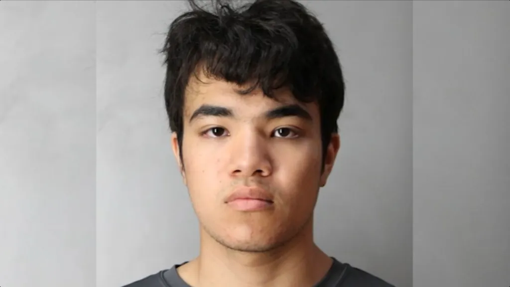 Mugshot of a young man with dark, messy hair and a neutral expression.