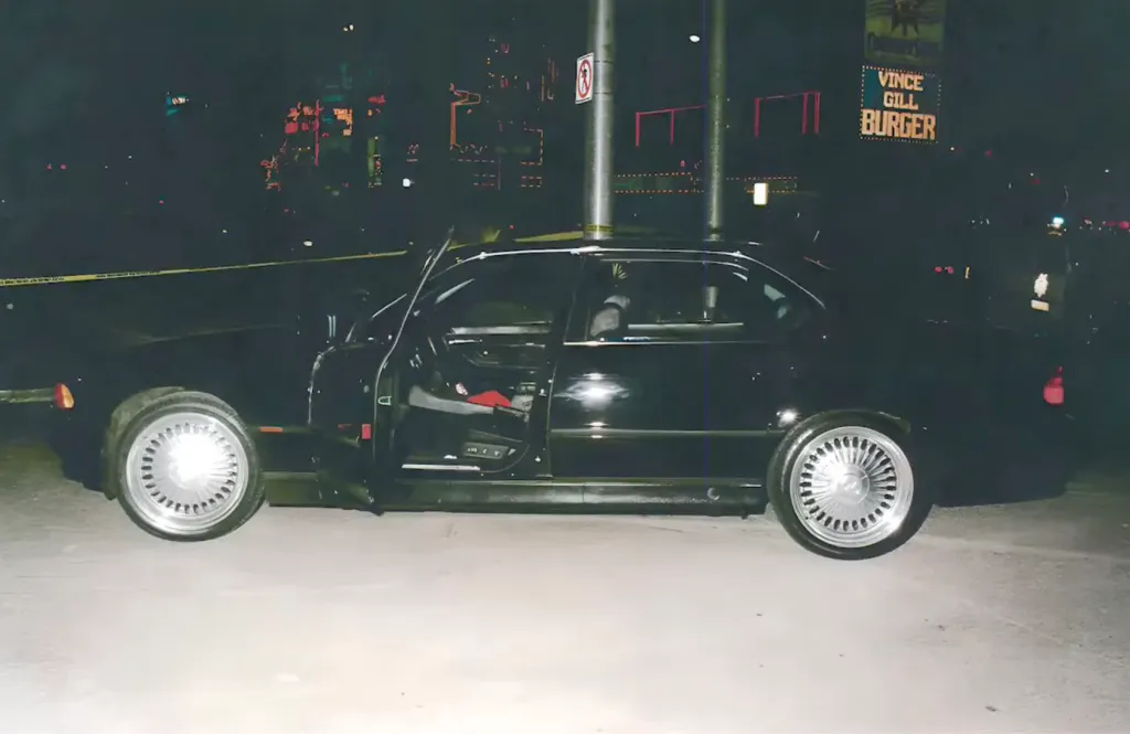 Scene of Tupac Shakur's shooting, showing a black car with the driver-side door open and yellow police tape in the background.