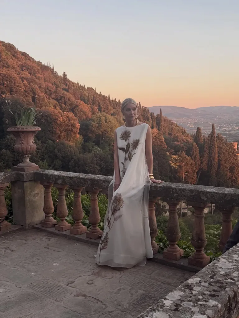 Gwyneth Paltrow on a balcony at sunset, overlooking a valley of trees and mountains.