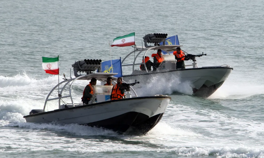 Two Iranian Revolutionary Guard speedboats, one with a machine gun, moving through water with flags.
