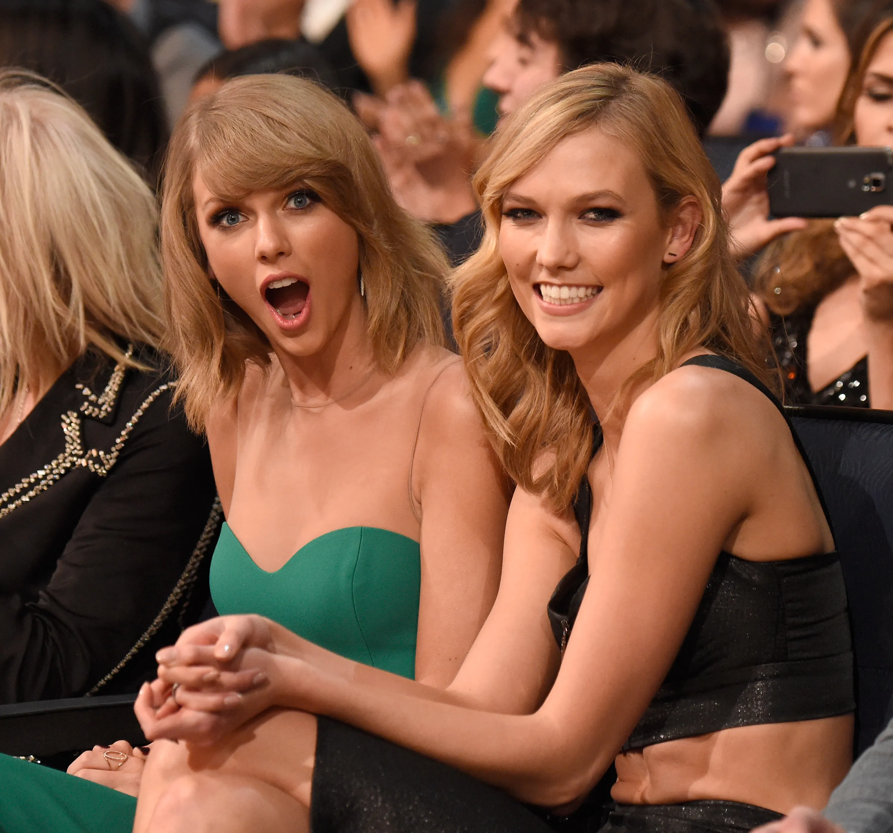 Taylor Swift, in a green dress with a sheer neckline, and Karlie Kloss, in a sparkly black top, sit next to each other at the American Music Awards.