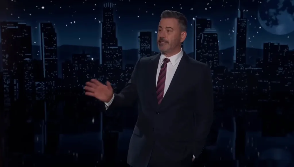 Jimmy Kimmel speaking on his late night show against a backdrop of a city skyline at night.