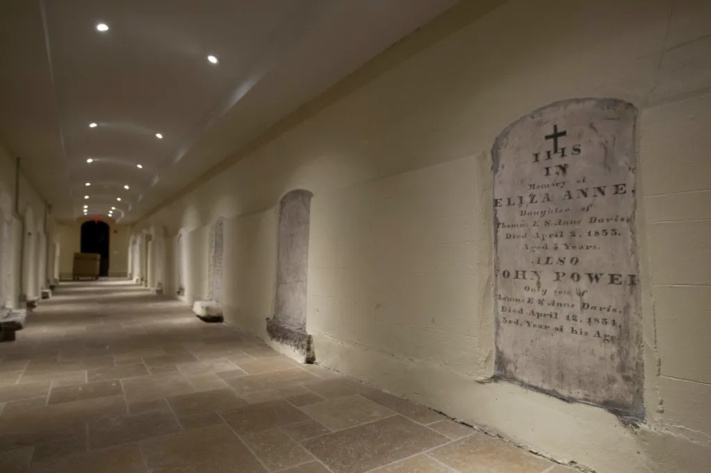 A crypt corridor with a tombstone embedded in the wall on the right.