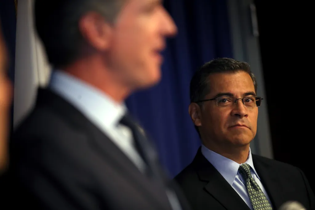 California Attorney General Xavier Becerra looking on as California Governor Gavin Newsom speaks.