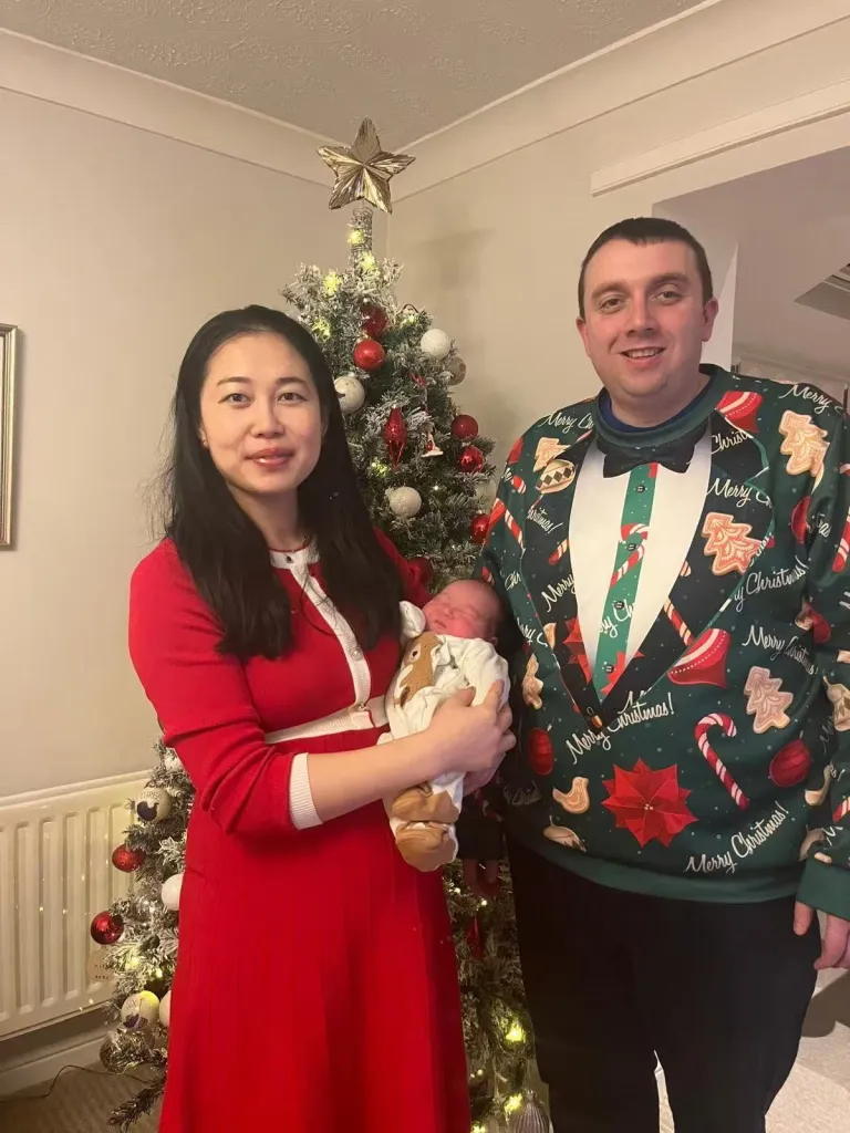 Leanne Zhang and Ben Donohoe with their newborn, posing in front of a Christmas tree.