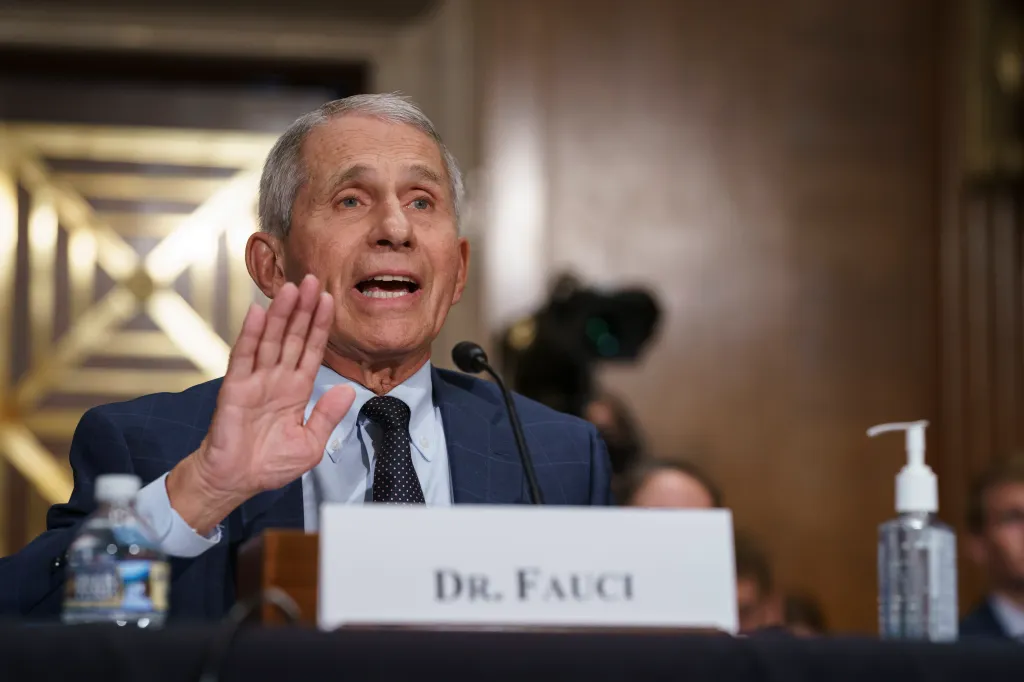 Dr. Anthony Fauci testifying before a Senate committee, hand raised as he speaks, with a microphone and 