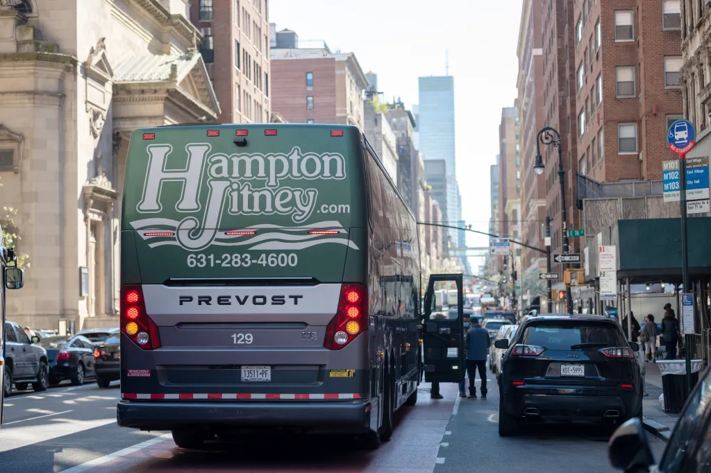 Back of a green Hampton Jitney bus, with an open door, on a city street in New York City.