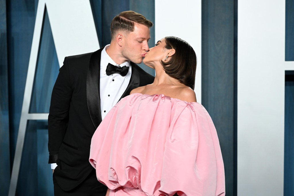 Christian McCaffrey in a tuxedo kissing Olivia Culpo in a pink off-the-shoulder gown.