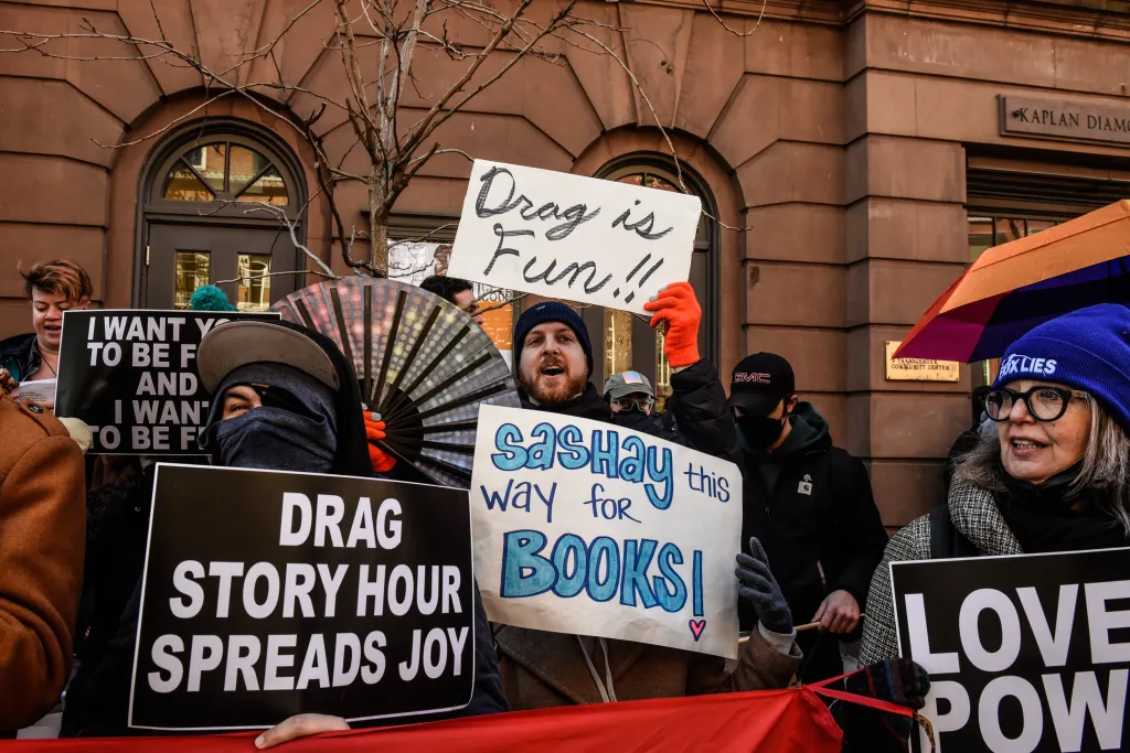 Protesters at a Drag Story Hour hold signs, one reads 