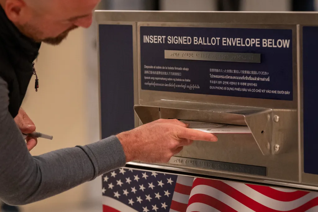A voter drops a ballot into a ballot drop box.