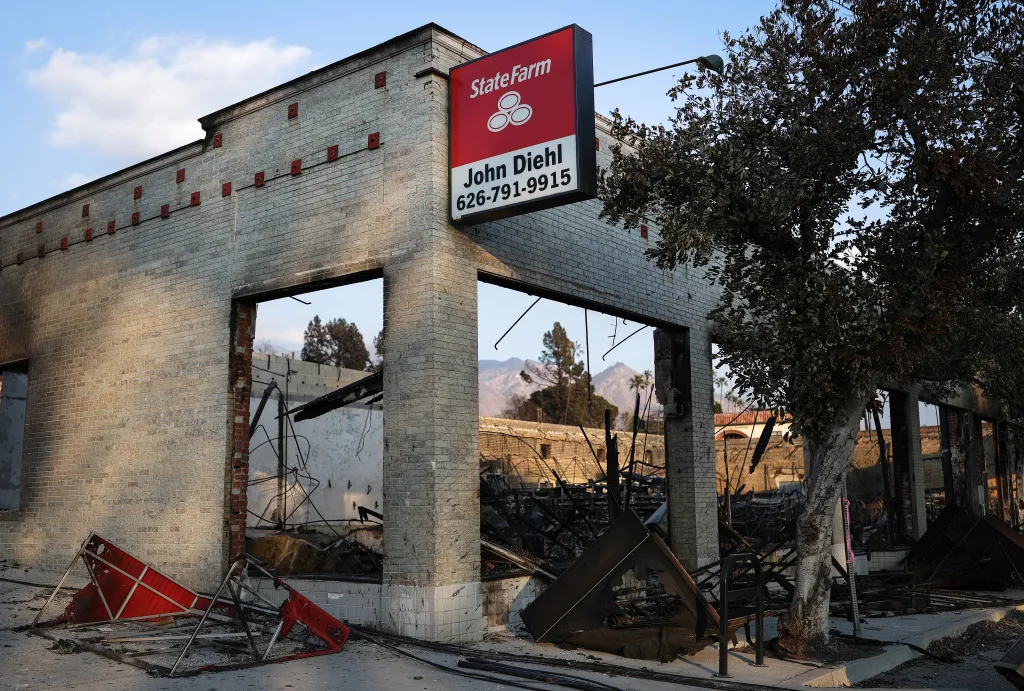 A State Farm office in Altadena, California, with a prominent red sign, stands severely damaged by fire, its windows gone and interior charred, following the Eaton Fire.