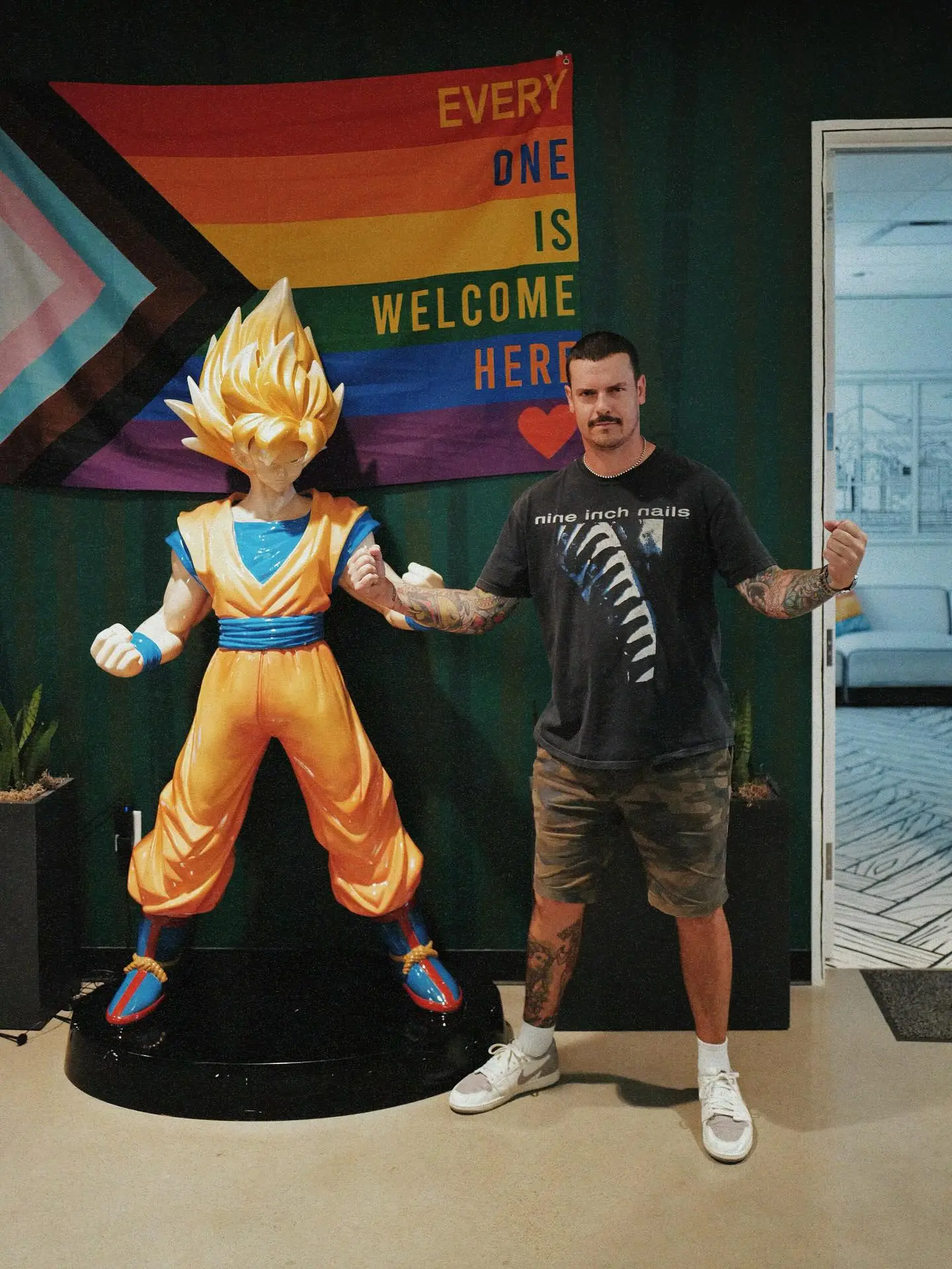 Caleb Shomo standing next to a Goku statue with a Pride flag behind them.