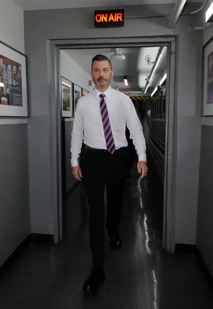 Jimmy Kimmel walks towards the camera in a hallway with an 