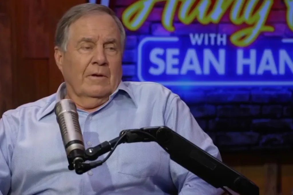 Bill Belichick speaking into a microphone with a neon 