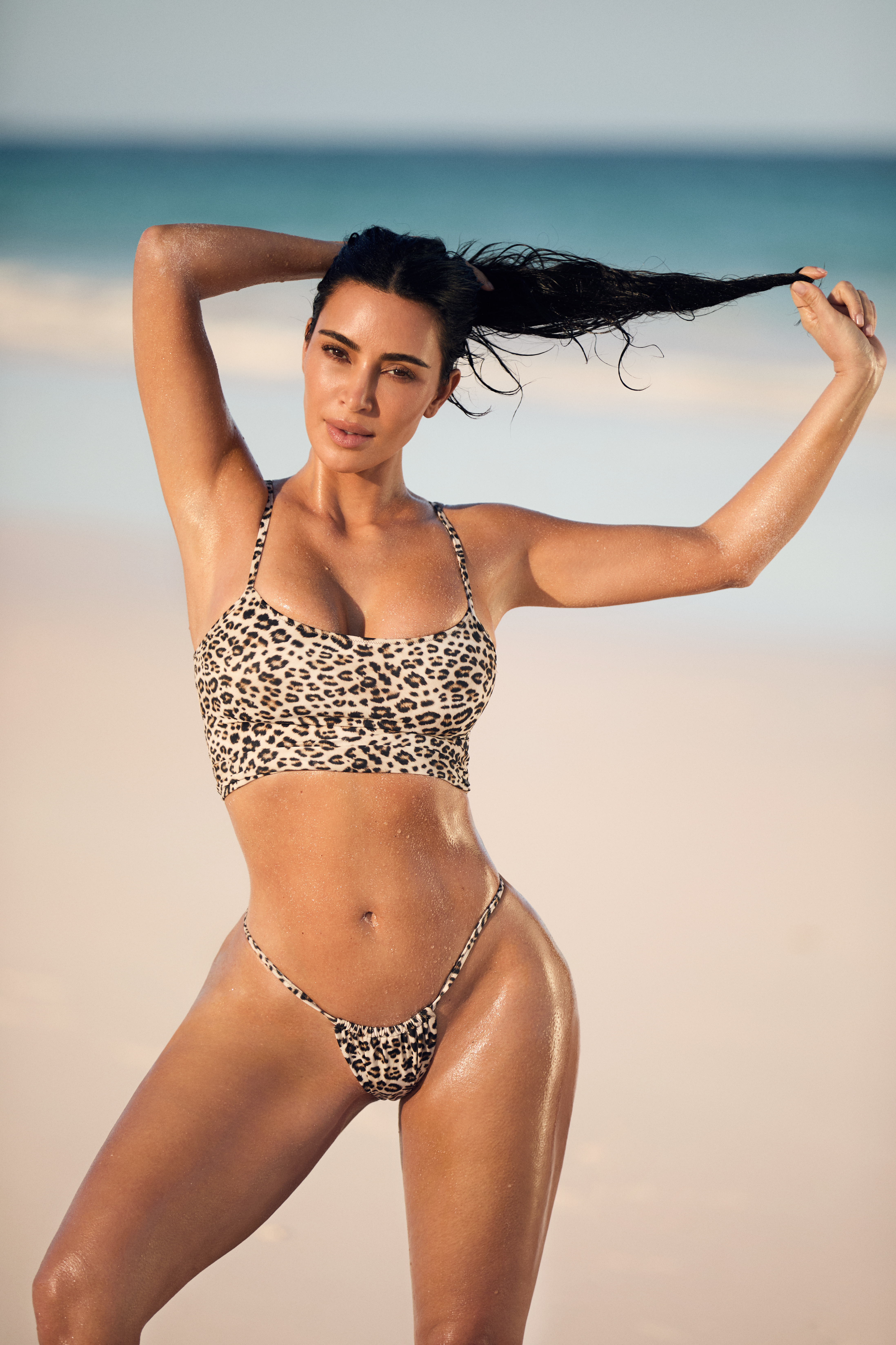 Kim Kardashian in a leopard print bikini, posing with wet hair on a beach.