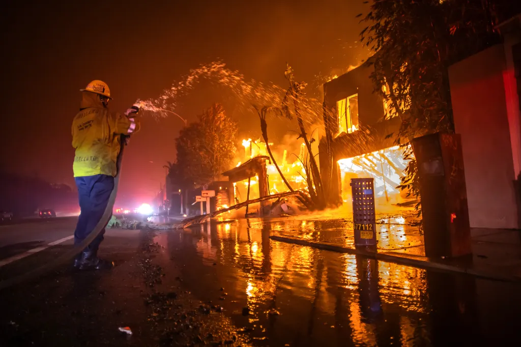 A firefighter battles the Palisades Fire while it burns homes at Pacific Coast Highway amid a powerful windstorm in Los Angeles, California.