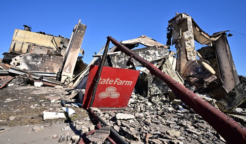 A red State Farm sign lies amidst the rubble of a building destroyed by the Palisades Fire.