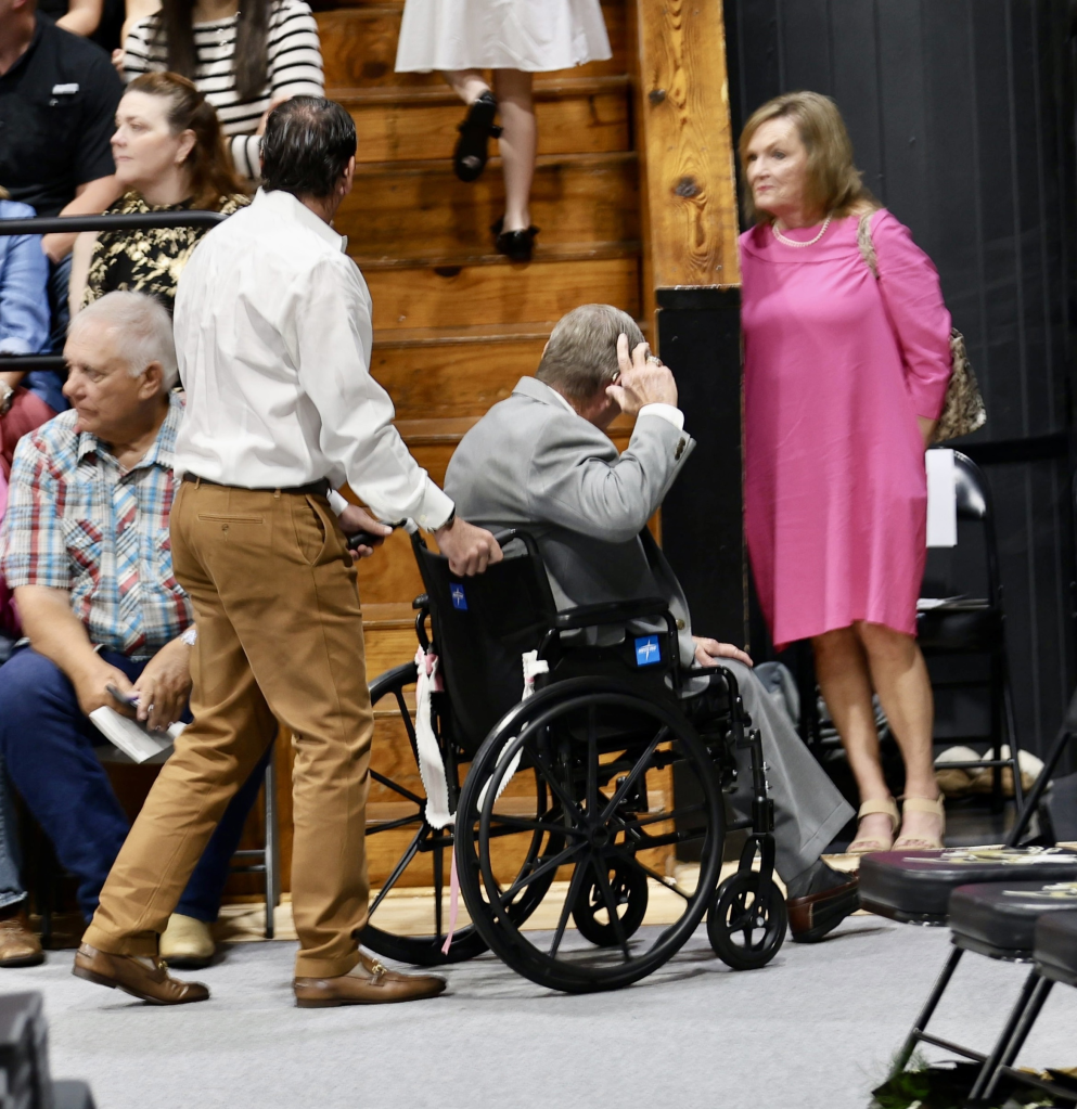 Jamie Spears in a wheelchair with someone pushing him from behind while Lynne Spears stands to the right, looking on.