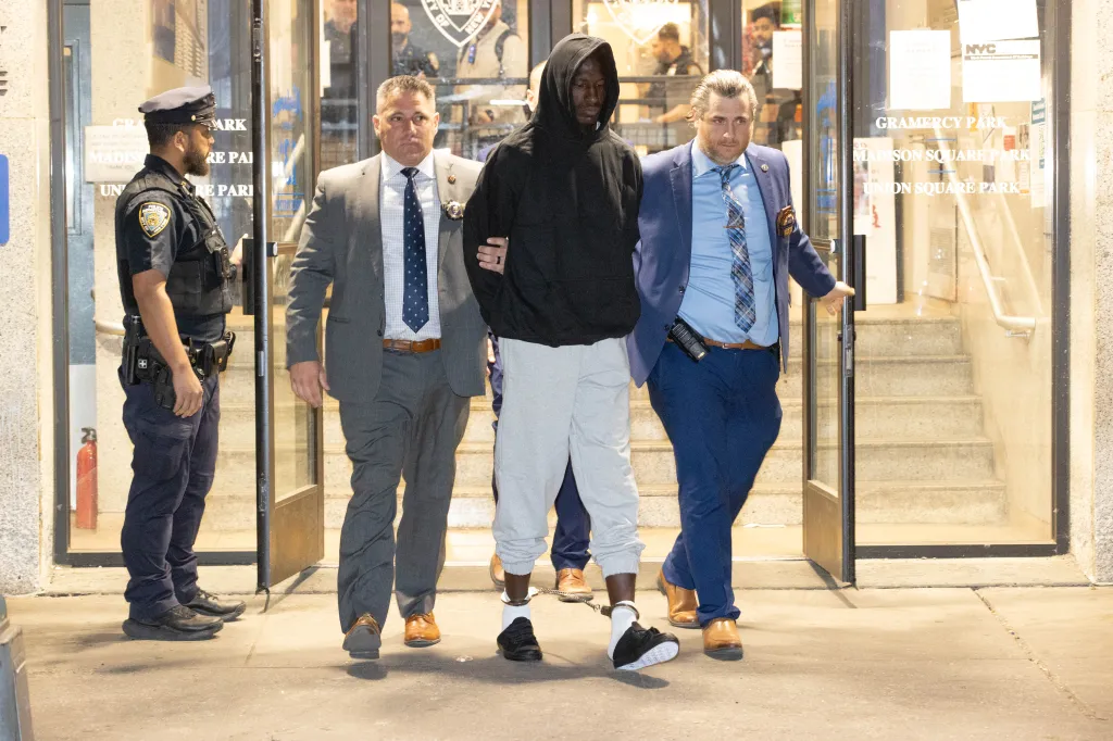Rhamell Burke, center, in handcuffs and ankle shackles, is led out of the 13th police precinct by two detectives and one police officer.