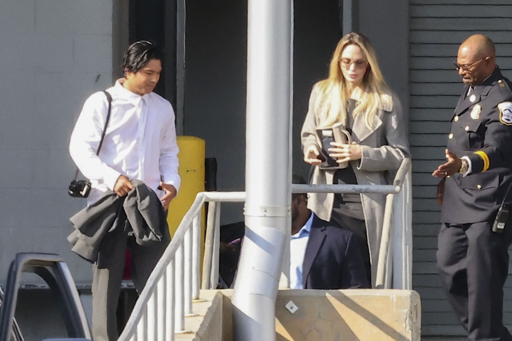 Angelina Jolie, in a light brown trench coat, with black skirt and grey sweater with Pax Jolie-Pitt in a white shirt and grey pants, holding a grey suit jacket.